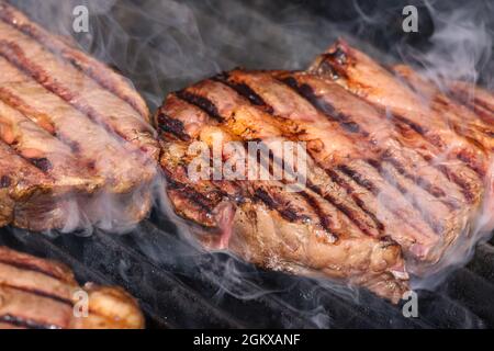 Close up searing and smoking ribeye beef steaks on open fire outdoor grill with cast iron metal grate, high angle view Stock Photo