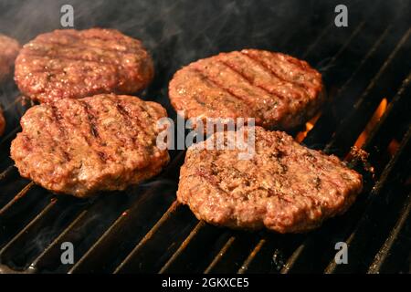 Close up searing and smoking beef or pork meat barbecue burgers for hamburger on bbq fire flame grill with cast iron metal grate, high angle view Stock Photo