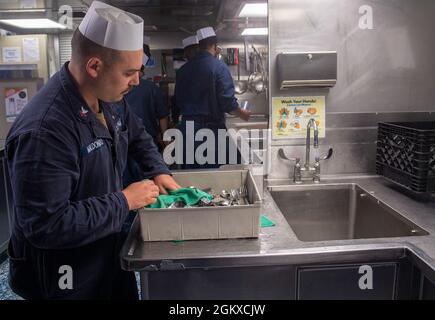 PACIFIC OCEAN (Jul. 17, 2021) Gunner’s Mate 2nd Class Joel Maldonado, from Acampo, Calif., washes dishes after chow on the mess decks aboard Independence-variant littoral combat ship USS Jackson (LCS 6). The Littoral Combat Ship (LCS) is a fast, agile, mission-focused platform designed to operate in near-shore environments, winning against 21st-century coastal threats. The LCS is capable of supporting forward presence, maritime security, sea control, and deterrence. Stock Photo