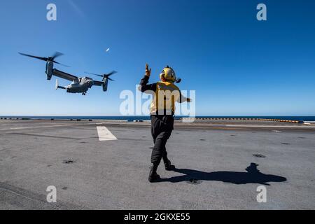 CORAL SEA (July 18, 2021) Aviation Boatswain’s Mate (Handling) Airman Elena Gurule, from Santa Fe, N.M., assigned to the forward-deployed amphibious assault ship USS America (LHA 6), signals an MV-22B Osprey from the 31st Marine Expeditionary Unit to land on the ship’s flight deck during Exercise Talisman Sabre 21. Talisman Sabre 21 is a large-scale, bilateral military exercise between Australia and the U.S. involving more than 17,000 participants from seven nations. Stock Photo