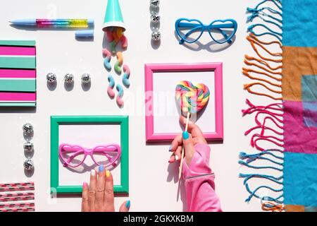 Birthday, holiday decor background. Sweets, chocolate, candy, sweet snacks. Hand with rainbow lollipop swirl. Tasty snacks and funny glasses in pink Stock Photo