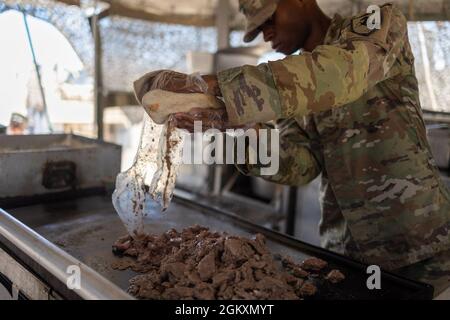 Spc. Courtney Roseborough, assigned to Regimental Support Squadron, 11th Armored Cavalry Regiment, moves a lunch entrée onto the grill top at the field feeding site, National Training Center and Fort Irwin, Calif., July 20th, 2021. He is part of the 11th Armored Cavalry Regiment field feeding team representing the National Training Center for the Philip A. Connelly Active Army Kitchen Competition. Stock Photo