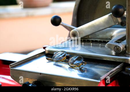 Slicing machine with eyeglasses. Spectacles on metal mechanical grocery knife. Vintage shop equipment. Calm reflection concept. Food supply. Closed Stock Photo