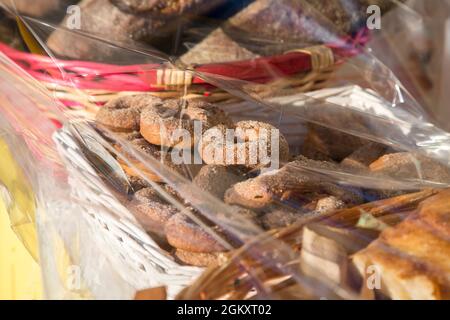 Homemade biscuits ciambelli with sugar on top and other bakery packed in baskets with transparent polyethylene film on the shell. Sweets in the market Stock Photo