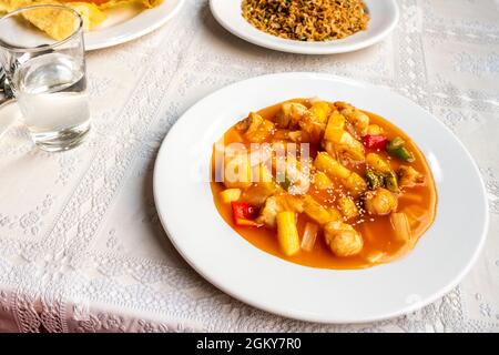 chinese recipe for chicken with pineapple and vegetables sautéed with sauce and sesame seeds with onions on white tablecloth in chinese restaurant Stock Photo