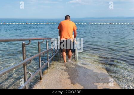 Disabled man on a wheelchair being transported into sea for swimming using a ramp.