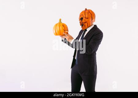 Man dressed in a suit jacket, blue tie and Jack-o-lantern pumpkin mask, speaking to an evil skull. Halloween and carnival celebration concept. Stock Photo