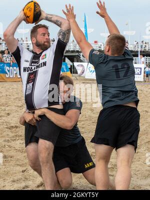 Sgt. Derek Dow, a team leader for Headquarters and Headquarters Company, 3rd Battalion “Dark Rifles,” 161st Infantry Regiment, tackles an opponent from behind as Pfc. Cody Hengeveld blocks the pass at the Sopot International Beach Rugby Tournament in Sopot, Poland, July 31, 2021. The Soldiers competed in the tournament to strengthen bonds with Polish locals and to increase ‘Dark Rifles’ interoperability. Stock Photo