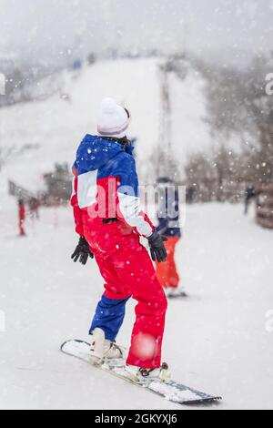 Back view close-up of girl snowboarder standing on ski slope in bright tracksuit. Winter holiday, sport concept Stock Photo
