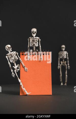 Blank orange notebook with skeletons on black background.Postcard for congratulations or invitations. Minimalistic holiday design for Halloween party. Stock Photo