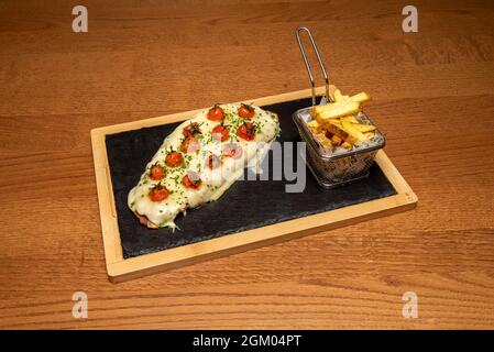 Milanese veal fillet with lots of cheese and cherry tomatoes with chives and a side of fried potatoes Stock Photo