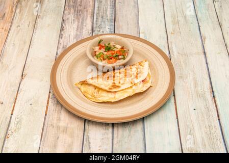 Mexican quesadilla with wheat tortilla stuffed with melted cheese and ham with pico de gallo and cilantro Stock Photo