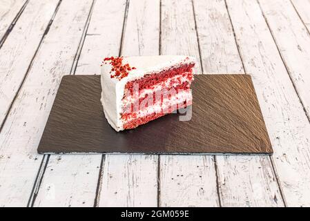 Red velvet cake portion with three layers of red sponge cake and two of white cream on a slate plate Stock Photo