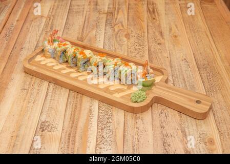 Uramaki dragon roll stuffed with prawns in tempura with sliced avocado, sauce, nori seaweed, fish roe, wasabi and ginseng Stock Photo