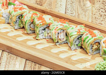 first course of sushi dragon roll uramaki stuffed with battered shrimp, nori seaweed, sliced ripe avocado, masago roe and sauce with wasabi and confit Stock Photo