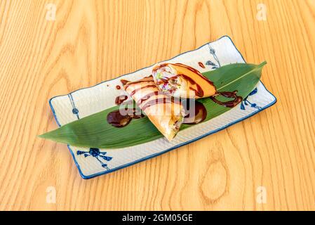 Delicious Asian crispy roll stuffed with vegetables on banana leaf and red sauce on wooden table Stock Photo