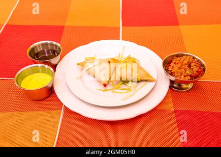 two vegetable samosas served in a Pakistani restaurant with sauces on an orange tablecloth Stock Photo