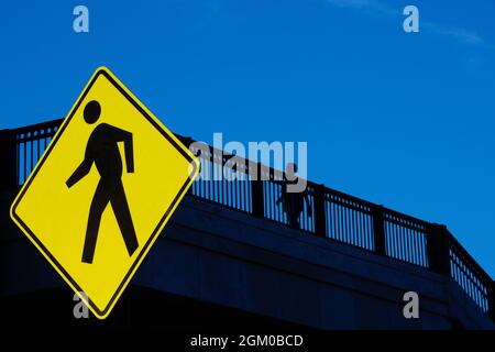 Silhouette of person walking on bridge with traffic walk sign Stock Photo