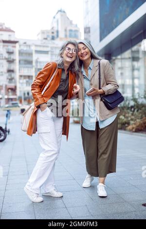 Stylish happy senior women stand on modern city street on autumn day Stock Photo