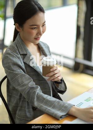Focused young businesswoman sit and work on desk while drinking coffee in office, asian business female worker working on laptop Stock Photo