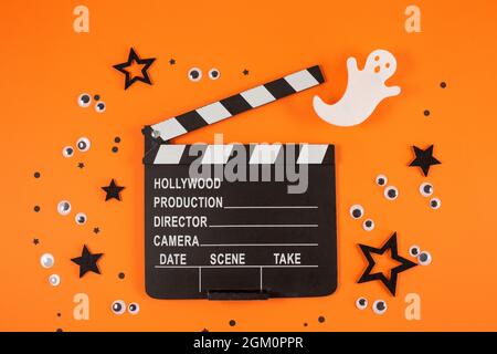 Clapper board in spider webs, spiders, ghost, eyes on orange background. Halloween horror movie concept. Flat lay composition. Top view Stock Photo