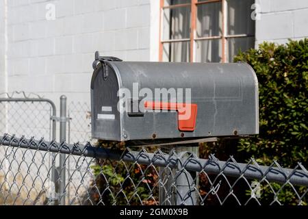 Closed US mailbox approved by the postmaster general with lowered red flag on wooden post next to chain link fence. Stock Photo