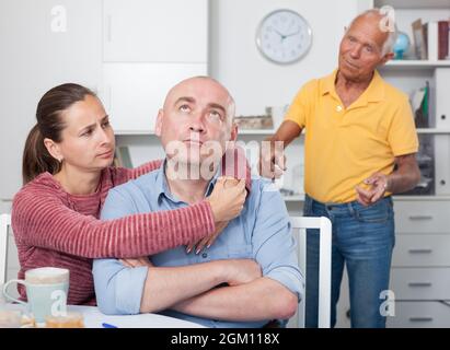 Couple hugging after conflict, worried elderly man on backgroud Stock Photo