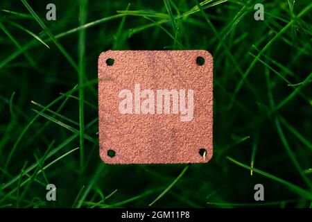 Top view of square brown leather patch for clothing creative layout of lawn green grass with logo tag Stock Photo