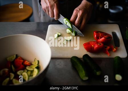 Cook cuts cucumbers for salad on a plastic board Stock Photo