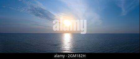 Panorama of sunrise on the sea. Small waves on the water and a cloudy sky with orange sun. Quiet morning rest on the beach Stock Photo