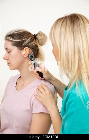 Otolaryngologist in turquoise medical uniform conducts examination using otoscope . Modern medical equipment. Medical examination. Latest technologies Stock Photo