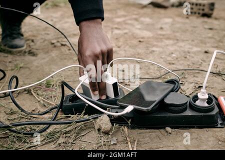 Close-up of unrecognizable black man plugging phone charger into socket on ground outdoors Stock Photo