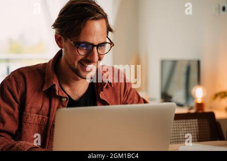 Caucasian male student working from home during lockdown typing on laptop at desk set up Stock Photo