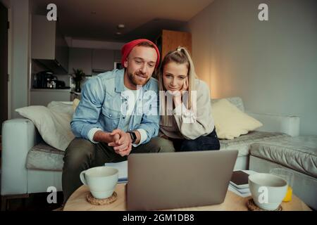 Caucasian happy couple sitting on sofa engaging in video call chatting to family Stock Photo