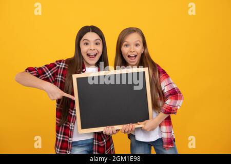 amazed kids in casual checkered point finger on school blackboard for copy space, advertisement Stock Photo