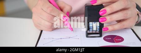 Woman holds pen and puts stamp on documents with business charts Stock Photo