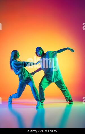 Young hip-hop dancers, stylish emotive girl and boy in action and motion in casual sports youth clothes on gradient multi colored background at dance Stock Photo