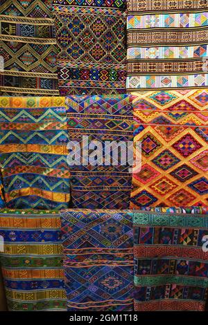 Vertical hanging display of vintage and modern Bhutanese woven and embroidered fabrics with bright colored patterns and designs in Thimphu Bhutan Stock Photo