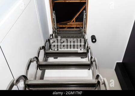 Metal stairs hidden in the ceiling to the attic with an opening hatch and folding stairs in the corridor, view from the bottom of the stairs up, moder Stock Photo
