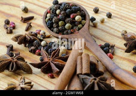 Still life of grains of different peppers in a wooden spoon, anise stars, cinnamon sticks and cloves on a wooden table. Selective focus. Macro. Stock Photo
