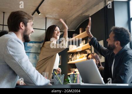Two cheerful young business people giving high-five while their colleagues looking at them and smiling. Stock Photo
