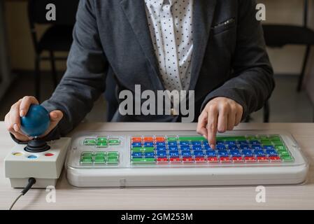 An unrecognizable woman with cerebral palsy is typing on the keyboard. A girl with disabilities works on a specially equipped computer Stock Photo