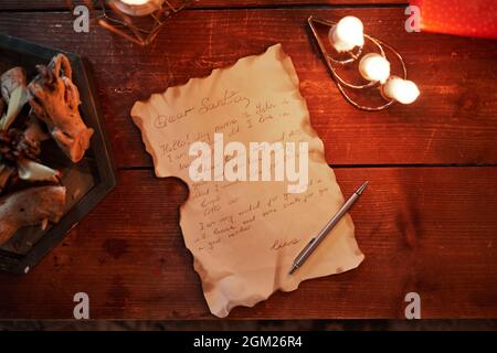 Directly above view of old letter with burnt edges, pen, candles on vintage wooden table Stock Photo