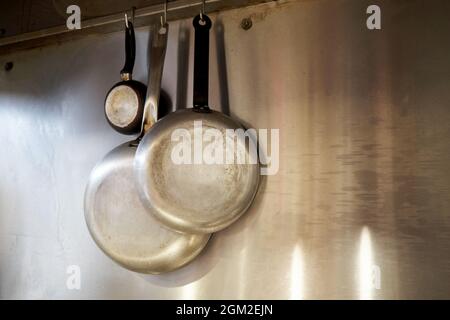Metal frying pans hanging on a rack in an industrial restaurant kitchen. Stock Photo