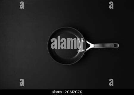Empty black frying pan on black wooden table background. Overhead top view with copy space. Stock Photo