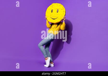 Full body portrait of satisfied person arms hold big emodji covering face isolated on purple color background Stock Photo