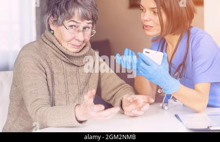 A nurse in a medical suit takes care and explains to an elderly patient Stock Photo