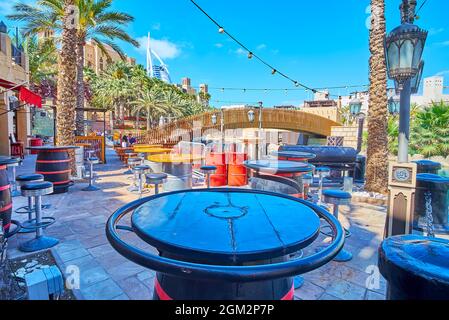 The outdoor cafe in Souk Madinat Jumeirah market complex with barrel-tables and tall palm trees in the background, UAE Stock Photo