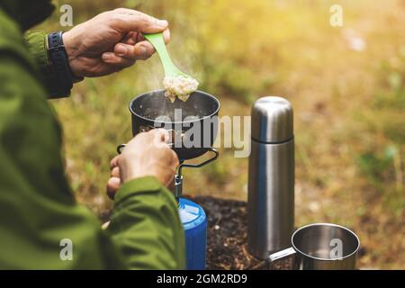 preparing oatmeal porridge outdoors on gas burner. camping cooking equipment Stock Photo