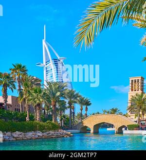 The tall green palms stretch along the canal of Souk Madinat Jumeirah market, the futuristic Burj al Arab is seen in the background, Dubai, UAE Stock Photo